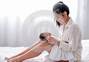 Asian mother put her newborn baby on her knees and sit on the bed, also look to the baby with carefully and love