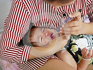 Asian mother`s arm wrapping around her crying baby girl`s face forcing the baby to take liquid medicine