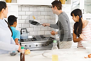 Asian mother, son and daughter watching father tossing pancake for breakfast in kitchen