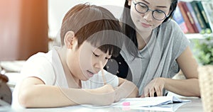 Asian mother with son doing homework in living room.