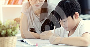 Asian mother with son doing homework in living room.