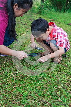 Asian mother and son exploring nature with magnifying glass. Hap