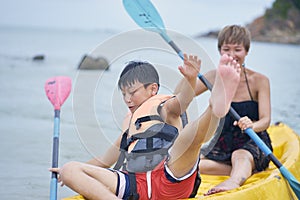 Asian mother and son playing kayaking on the sea during vacation when kid losing balance