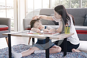 Asian mother take care a little girl child is drawing and painting with wooden colored pencils on paper together in living room.