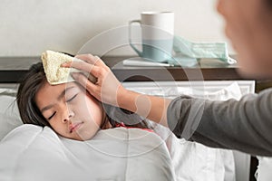 Asian mother take cool towel for reduce high fever on sick girl forehead on bed at morning time, Selective focus, Healthy and