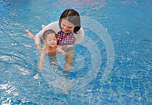 Asian mother take little Asian baby boy in swimming class. Happy toddler enjoying swim in pool with mom