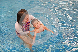 Asian mother take little Asian baby boy in swimming class. Happy toddler enjoying swim in pool with mom