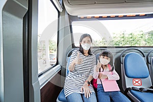 asian mother taking her daughter to school by riding bus public transport wearing a face mask