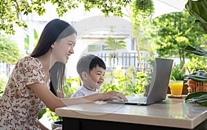 Asian mother teach her son by note book computer in garden at home