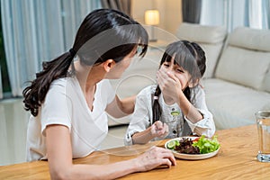 Asian Mother teach and motivate young girl child eat green vegetable. Small kid daughter smell on cucumber on dinner plate with