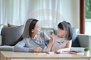 Asian mother teaching her cute kid daughter to studying in living room