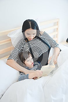 Asian mother teaching her daughter to reading a bed time story book in holiday