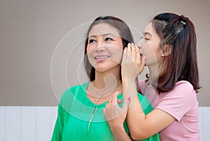 Asian mother and teen daughter whispering gossip