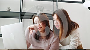 Asian mother and teenage daughter looking at laptop computer at home office