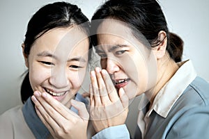 Asian mother whispering gossiping in her daughter ear,adult woman look at other with disdain,aversion,telling a secret to photo