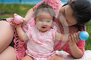 Asian mum and little child - young happy and beautiful Chinese woman playing on city park with adorable and cheerful baby girl in