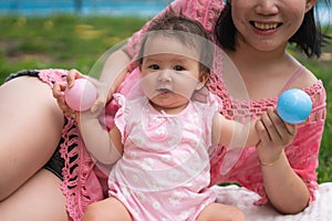 Asian mum and little child - young happy and beautiful Chinese woman playing on city park with adorable and cheerful baby girl in