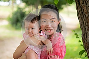 Asian mum and little child - young happy and beautiful Chinese woman playing on city park with adorable and cheerful baby girl in