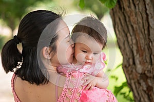 Asian mum and little child - young happy and beautiful Chinese woman playing on city park with adorable and cheerful baby girl in