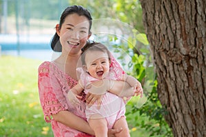 Asian mum and little child - young happy and beautiful Chinese woman playing on city park with adorable and cheerful baby girl in