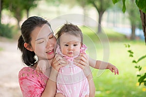 Asian mum and little child - young happy and beautiful Chinese woman playing on city park with adorable and cheerful baby girl in