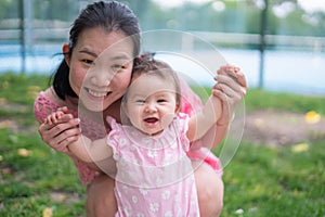 Asian mum and little child - young happy and beautiful Chinese woman playing on city park with adorable and cheerful baby girl in