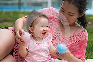 Asian mum and little child - young happy and beautiful Korean woman playing on city park with adorable and cheerful baby girl in