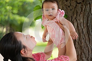 Asian mum and little child - young happy and beautiful Korean woman playing on city park with adorable and cheerful baby girl in