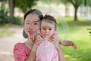 Asian mum and little child - young happy and beautiful Korean woman playing on city park with adorable and cheerful baby girl in