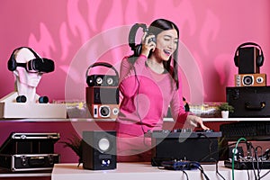 Asian musician with headphones playing electronic song at mixer console