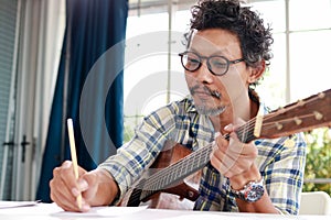 Asian musician playing guitar is composing. Music teacher.