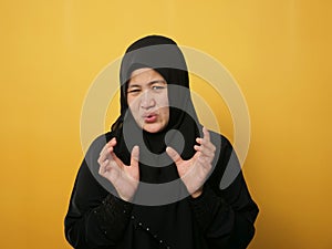 Asian musim woman afraid expression with hands raised up, surrender gesture, over yellow background