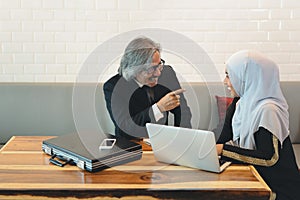 Asian muslim business man having meeting with business woman who using laptop computer on wooden desk in coffee shop