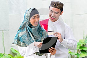 Asian Muslim couple shopping online on pad in living room