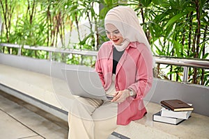 An Asian Muslim female college student using her laptop, doing her school project