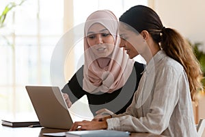 Asian muslim female mentor teaching caucasian intern explaining computer work