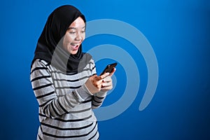 Asian muslim girl wearing hijab smiling while browsing trough internet or reading chat message on her phone