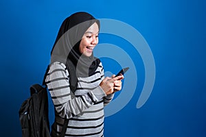 Asian muslim girl wearing hijab smiling while browsing trough internet or reading chat message on her phone