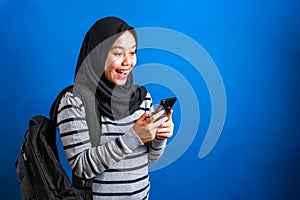 Asian muslim girl wearing hijab smiling while browsing trough internet or reading chat message on her phone