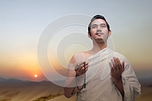 Asian Muslim man in ihram clothes praying with prayer beads on his hands