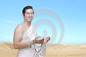 Asian Muslim man in ihram clothes praying with prayer beads on his hands