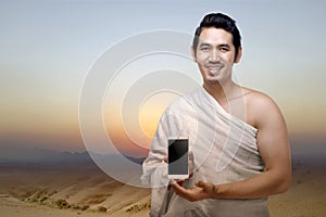 Asian Muslim man in ihram clothes showing a mobile phone