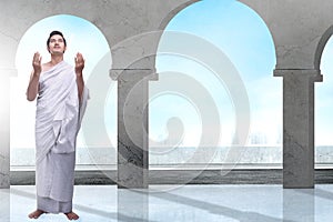 Asian Muslim man in ihram clothes standing and praying while raised arms