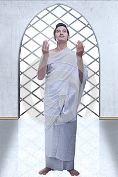 Asian Muslim man in ihram clothes standing and praying while raised arms