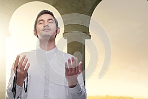 Asian Muslim man standing and praying with prayer beads while raised arms