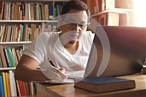 Asian muslim man studying in library, exam preparation concept. Male college student using laptop to learn online