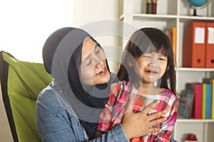 Asian muslim mother hijab calming her sad and crying daughter, single mom and baby girl together