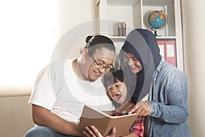Asian muslim parent, mother, father and child are reading a book at home, happy excited expression photo