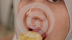 Asian muslim woman enjoys eating casava or potato chips while sitting on sofa at living room, close up