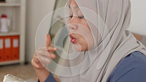 Asian muslim woman enjoys eating hot spicy casava or potato chips while sitting on sofa at living room, close up